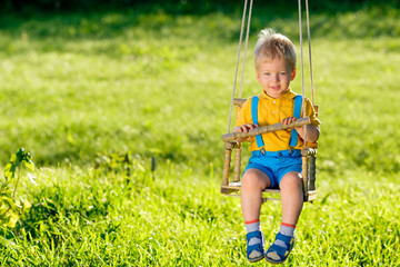 Rural scene with toddler boy swinging outdoors.