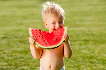 One year old baby boy eating watermelon in the garden
