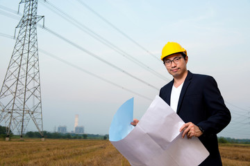 An engineer wear yellow hard hat and suite hold blueprint in hand standing on field looking at...