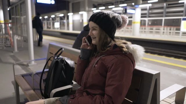 Happy teenage girl talking on cellphone while waiting for train at night
