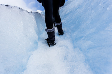 Woman walking with hiking acessories, on top of large ice glacie