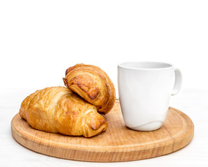 Cutting board with cup of coffee and two croissants on the table. Isolated on white.