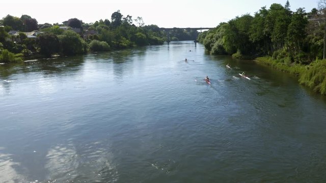 Moving drone shot of adults rowing down blue river.