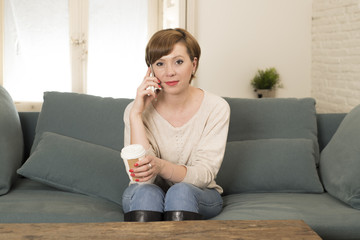 young attractive and happy red hair woman sitting at home sofa couch drinking coffee talking on mobile phone relaxed in communication concept