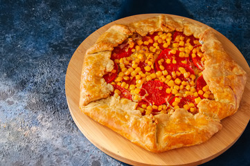 Tomato and sweet corn galette on a wooden board. Top view. Blue stone background.