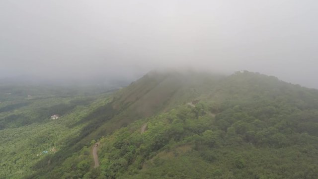 A cinematic shot of a mountain top covered in mist with a curvaceous road in the frame.