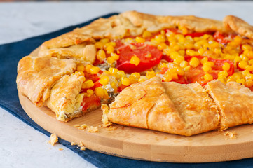 Tomato and sweet corn galette on a wooden board. Close up. White stone background.