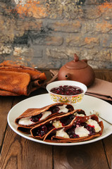 Chocolate crepes (blinis) with sour cream and black currant sauce on a white plate. Wooden...