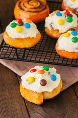 Classic cinnamon rolls - cinnabons with cream cheese frosting with smarties. Wooden background.