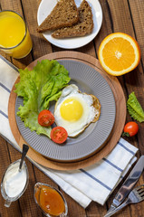 English Breakfast: fried egg, juice, cherry tomatoes, lettuce, grain bread, sauce, top view.