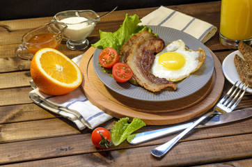 English Breakfast: fried egg with bacon, orange juice, tomatoes, zernovoi bread, lettuce leaf, top view.