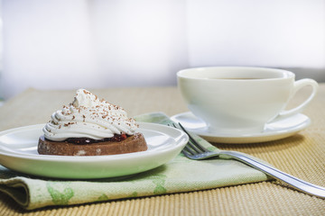 A cup of tea, pieces of chocolate and a chocolate cake with egg white cream closeup