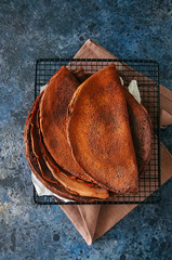 Chocolate crepes (blinis) on a wire racke. Blue stone background. Top view