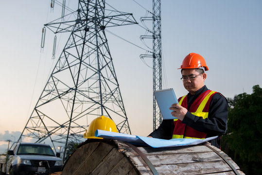 Electrical engineer working. Electrician holding tablet at high voltage power pylon against blue sky