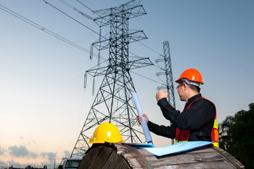 Electrical engineer working. Electrician holding blueprint at high voltage power pylon against blue sky