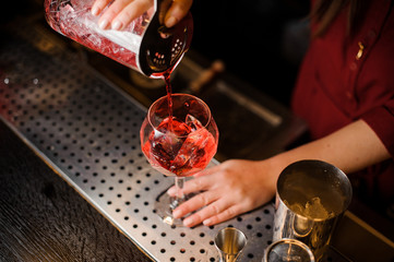 Female barman hands pouring sweet red alcoholic drink into a glass