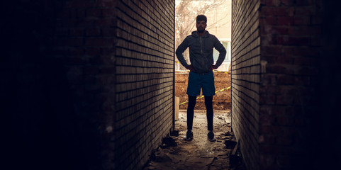 Portrait of focused motivated afro-american young handsome hipster man with earphones standing inside of the abandoned place in the middle of two walls.