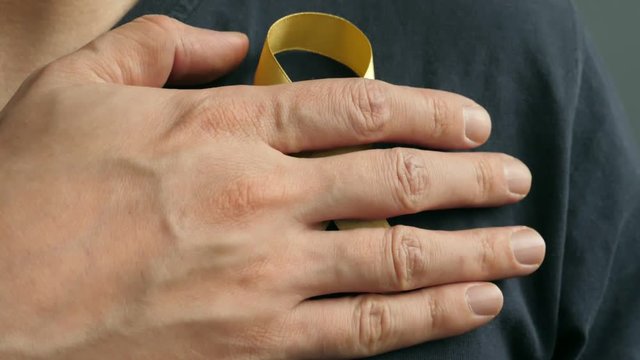 A man attaches a gold or yellow awareness ribbon to his shirt.