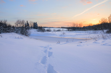 Frosty winter landscape with frozen river.Twilight.Cold morning.Snow covered trees.Sunrise.Footprints in drifts.River Torgosha in Moscow region,Russia.
