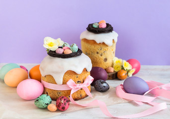 Obraz premium Colorful Easter spring stillife in soft light and trendy pastel colors. Traditional cake with chocolate nest, candy and qail eggs decoration blossom flowers on violet background