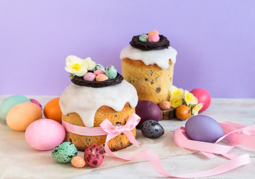 Colorful Easter spring stillife in soft light and trendy pastel colors. Traditional cake with chocolate nest, candy and qail eggs decoration blossom flowers on violet background