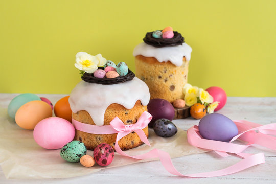 Colorful Easter spring stillife in soft light and trendy pastel colors. Traditional cake with chocolate nest, candy and qail eggs decoration blossom flowers on green background