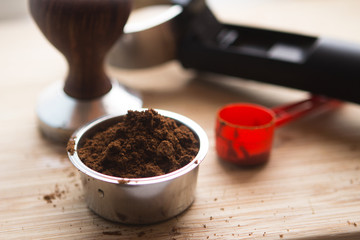 coffee tamper with coffee in filter basket and filter holder on a wooden board for coffee scrub