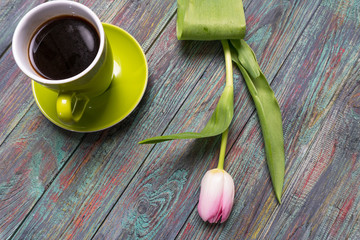 A cup of coffee and pink tulips flowers on wooden background.