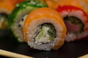Bright sushi rolls with red salmon, cheese, rice, caviar on black background