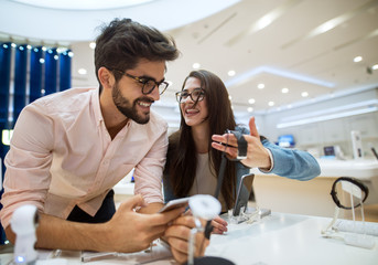 Close up portrait view of cute happy satisfied hipster young love couple holding and testing new smart gadgets in a tech store.