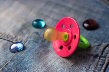 Baby pacifier with colored stones on blue jeans