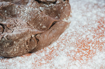 Chocolate dough for cakes on a wooden board, sprinkled with wheat flour closeup