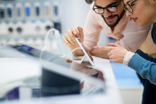 Close up side view of curious charming happy young student love couple pointing to a new tablet in a tech store.