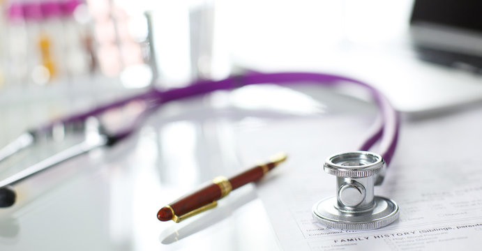 closeup of the desk of a doctors office with a stethoscope in the foreground and a bottle with pills in the background