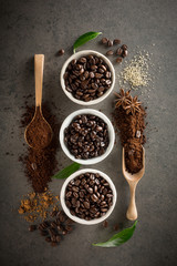 Different varieties of coffee beans with sugar and green leaf on dark vintage background. From top view