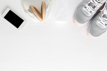 Flat lay of fitness accessories on white wooden background. Running shoes, towel, smartphone and headphone from top view.