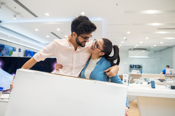 Obraz premium Close up portrait view of pretty happy excited hipster young love couple looking each other and holding a box of new smart gadgets after buying in a tech store.
