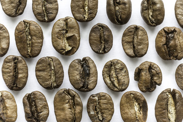 Rows of roasted coffee beans. Different shapes and different shades of brown. On a white background. Site about food, drinks, health, business.
