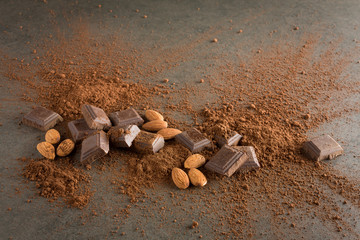 Broken chocolate pieces with cocoa powder and almond on stone background