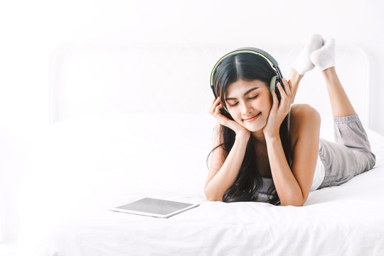 Woman listening music with headphones on bed