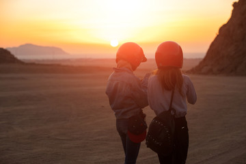 Women tourists with helmet, morning sunrise in desert, rear view, looking smartphone