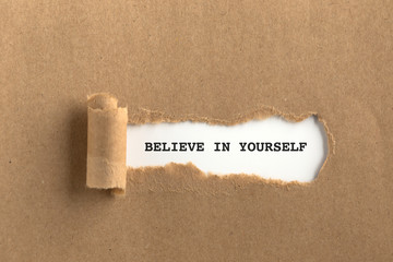 The text BELIEVE IN YOURSELF behind torn brown paper
