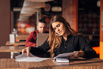 Happy businesswoman sitting at the table and talking on the phone in cafe.bearded freelancer in the background