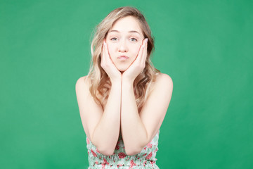 Young adorable blonde female expresses her love, blows kiss at camera, isolated over green wall background. Pretty woman flirts with handsome guy. People, body language and facial expressions concept.