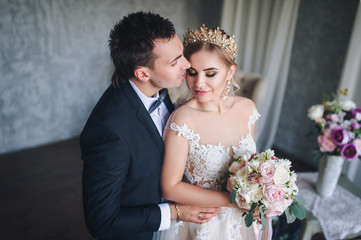 The groom tenderly embrace his bride. Blonde in a lace dress. Precious jewelry of the bride.