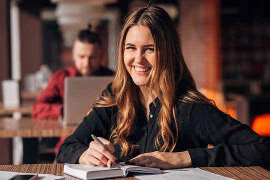 Portrait of a confident woman taking notes in a notepad while sitting at the table in a cafe indoors and looking at camera