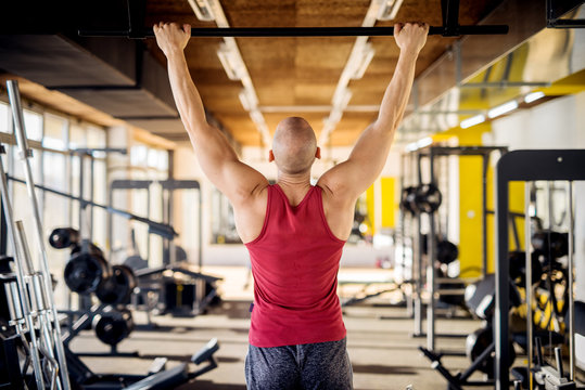Close up back view of motivated and focused strong muscular active healthy young bald man working pull ups in the modern gym.