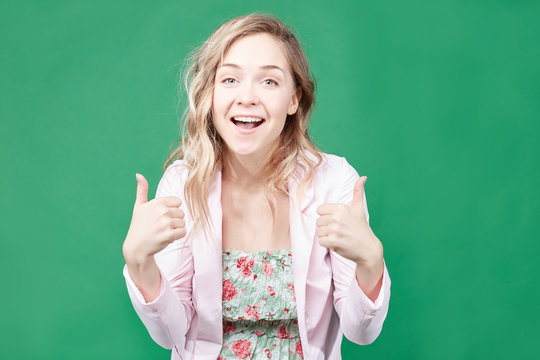 Portrait of young Caucasian female employee or customer with ultra white wide smile, looking at  camera with happy expression, showing thumbs-up with both hands, achieving career goals. Body language