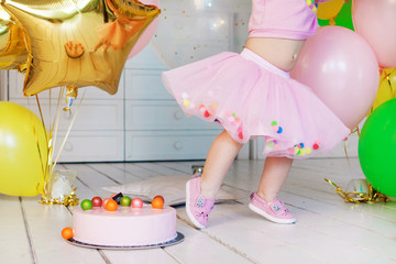  Little girl in a pink fluffy skirt. Pink mousse cake with colorful balls on a white wooden floor