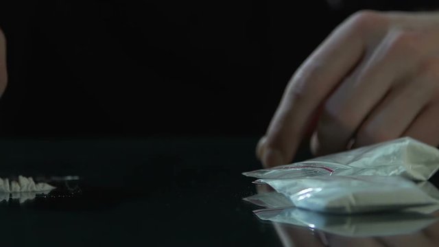 Drug dealer making cocaine lines by card with drug packages on table, addiction